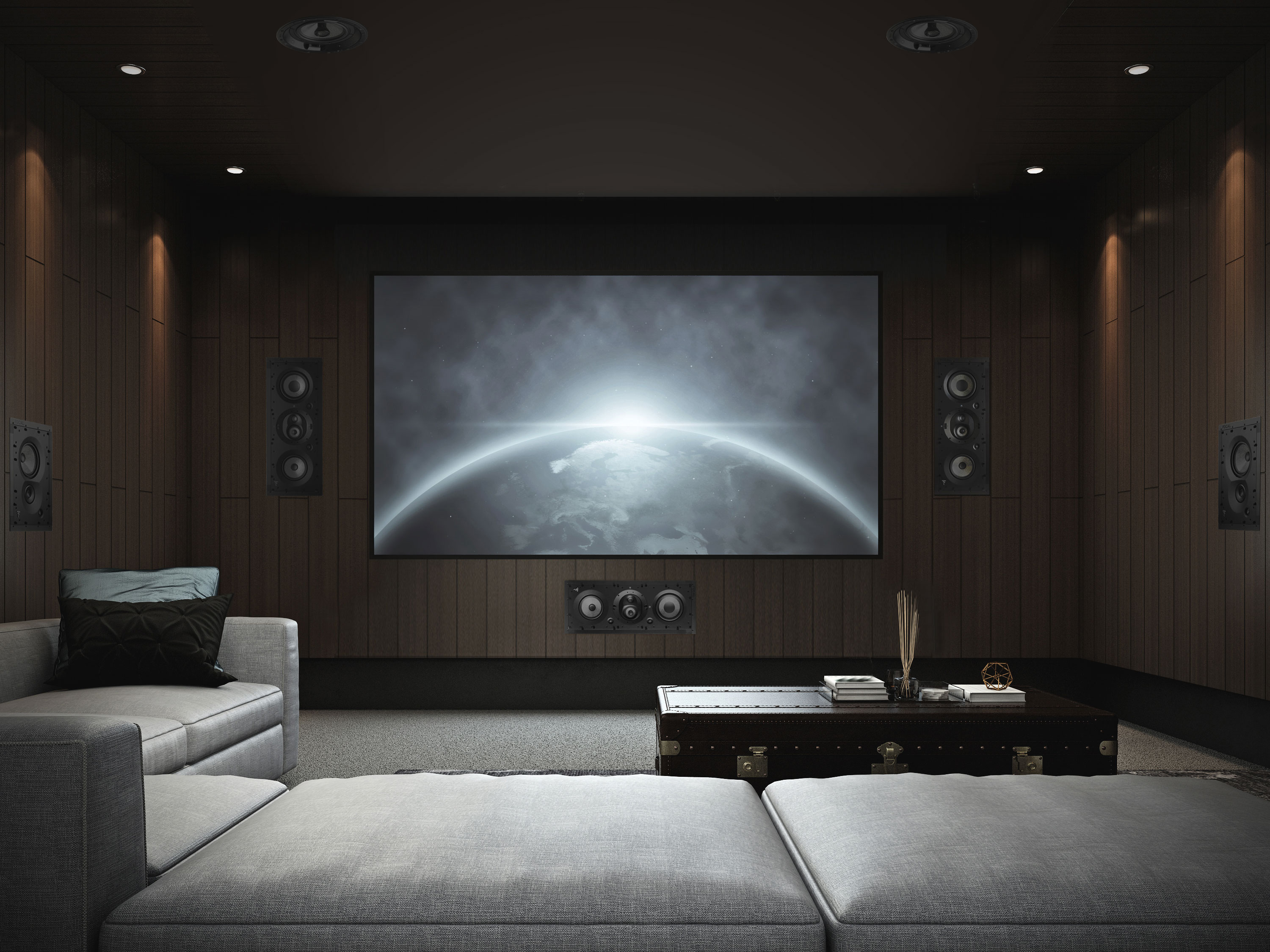 Dark home theater room with a large screen showing a space scene, built-in surround speakers, and gray sectional seating.