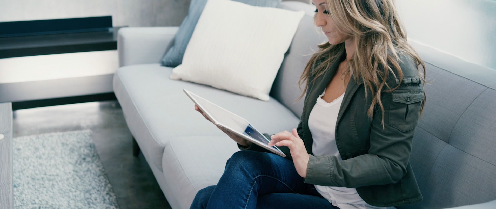 Woman using a tablet to control her smart home while relaxing on the couch